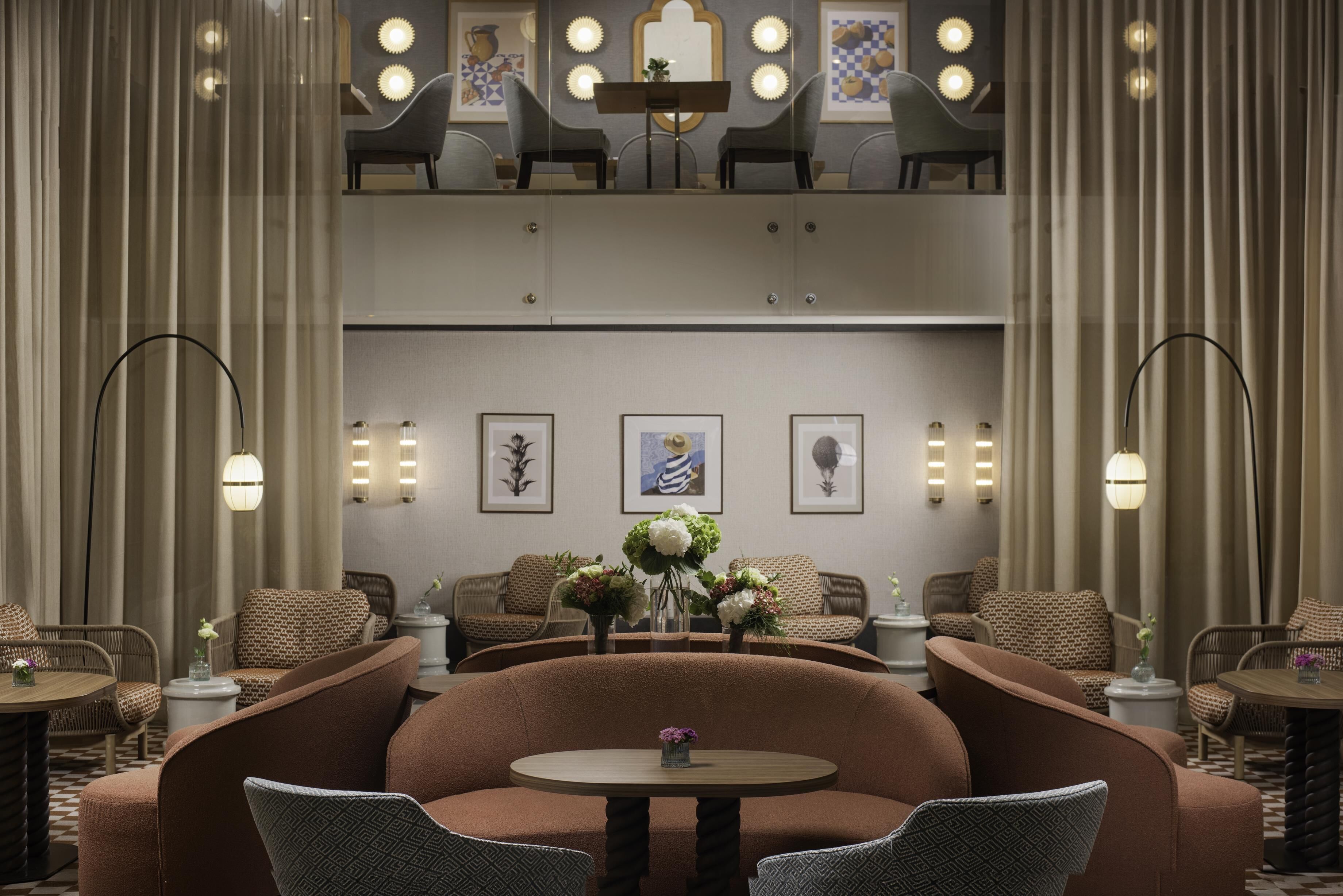 A hotel lobby with a central seating area, framed artwork on the walls, and a chandelier.