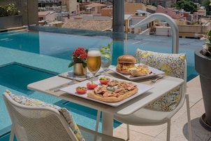 A dining table with a meal, a drink, and a poolside view.