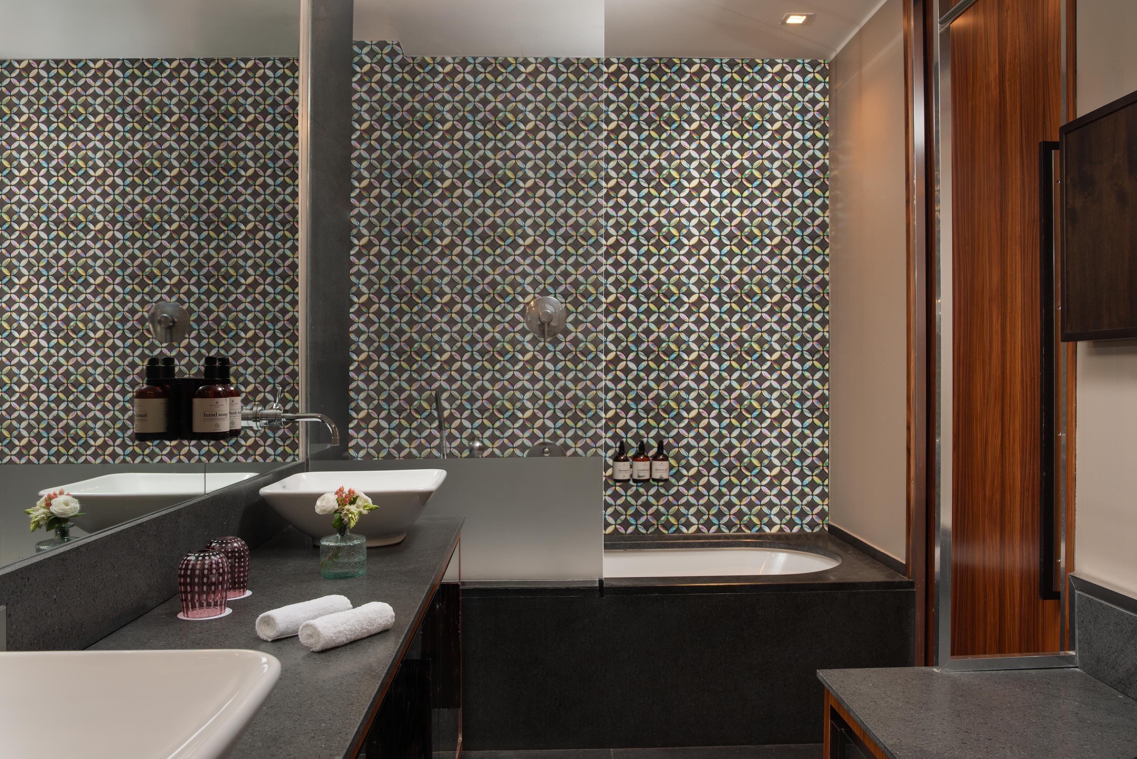 Ein modernes Badezimmer mit zwei Waschbecken, einer Badewanne und einer Dusche. Auf der Ablage befinden sich dekorative Vasen und Flaschen.