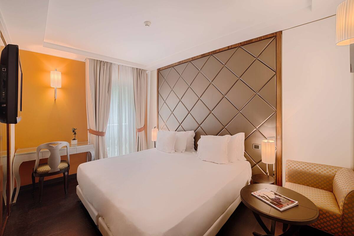 A hotel room with a large bed, a desk with a chair, a sofa, and a TV.