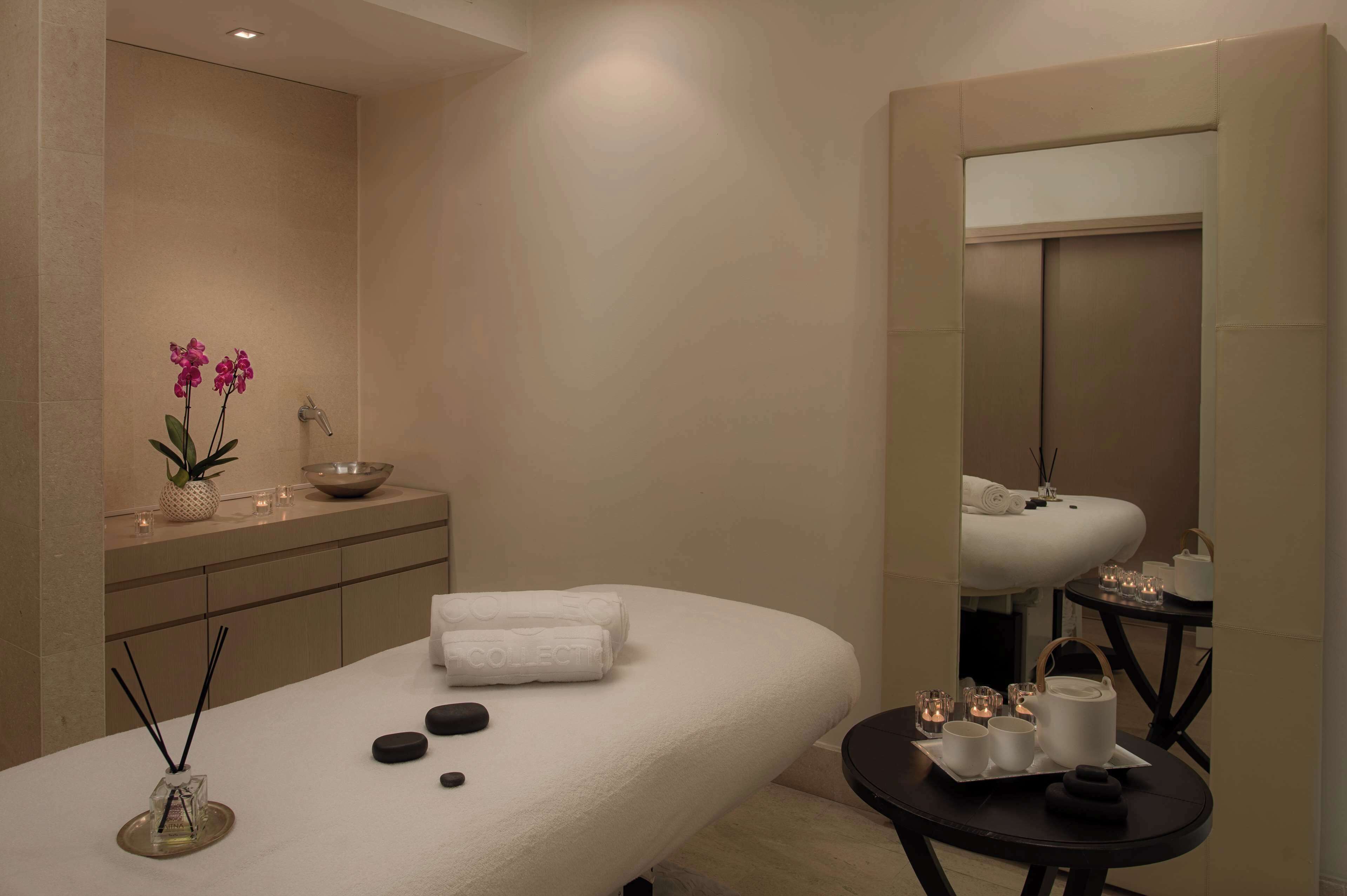 A spa room with a massage table, candles, a small table with tea sets, and a mirror.