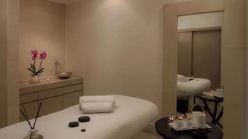 A spa room with a massage table, candles, a small table with tea sets, and a mirror.
