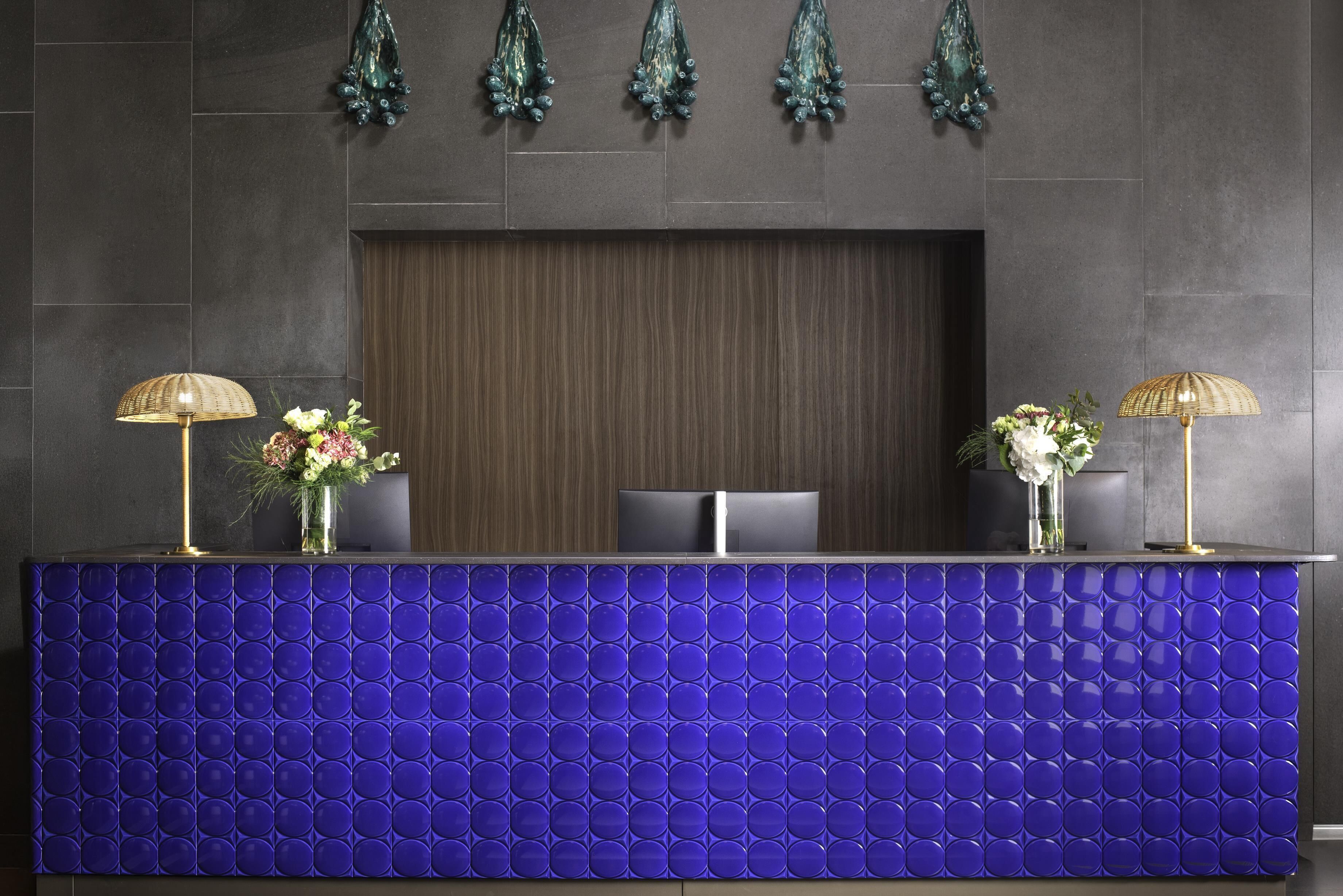 A reception desk with a blue tiled front, two lamps, and two vases with flowers.