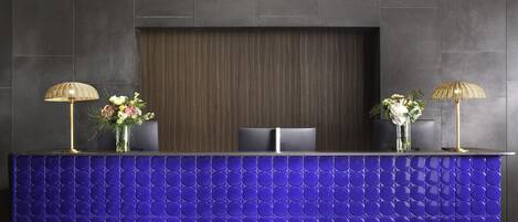 A reception desk with a blue tiled front, two lamps, and two vases with flowers.