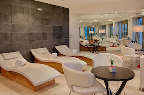 A modern spa area with reclining chairs, a small table with a plant, and a mirror reflecting the room. - NH Collection Taormina (Taormina)