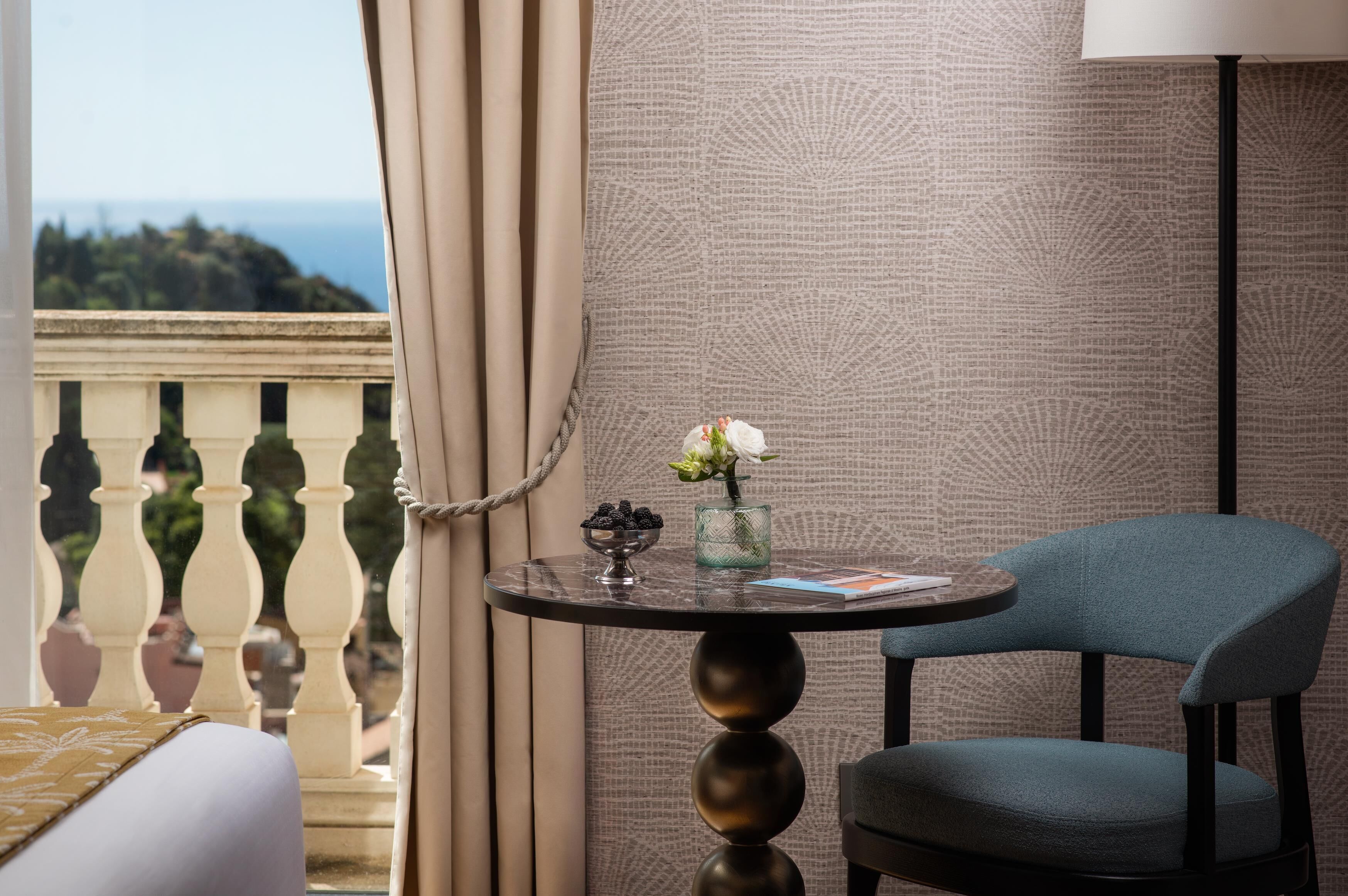 A balcony with a view of the sea, a table with a vase of flowers, and a chair.