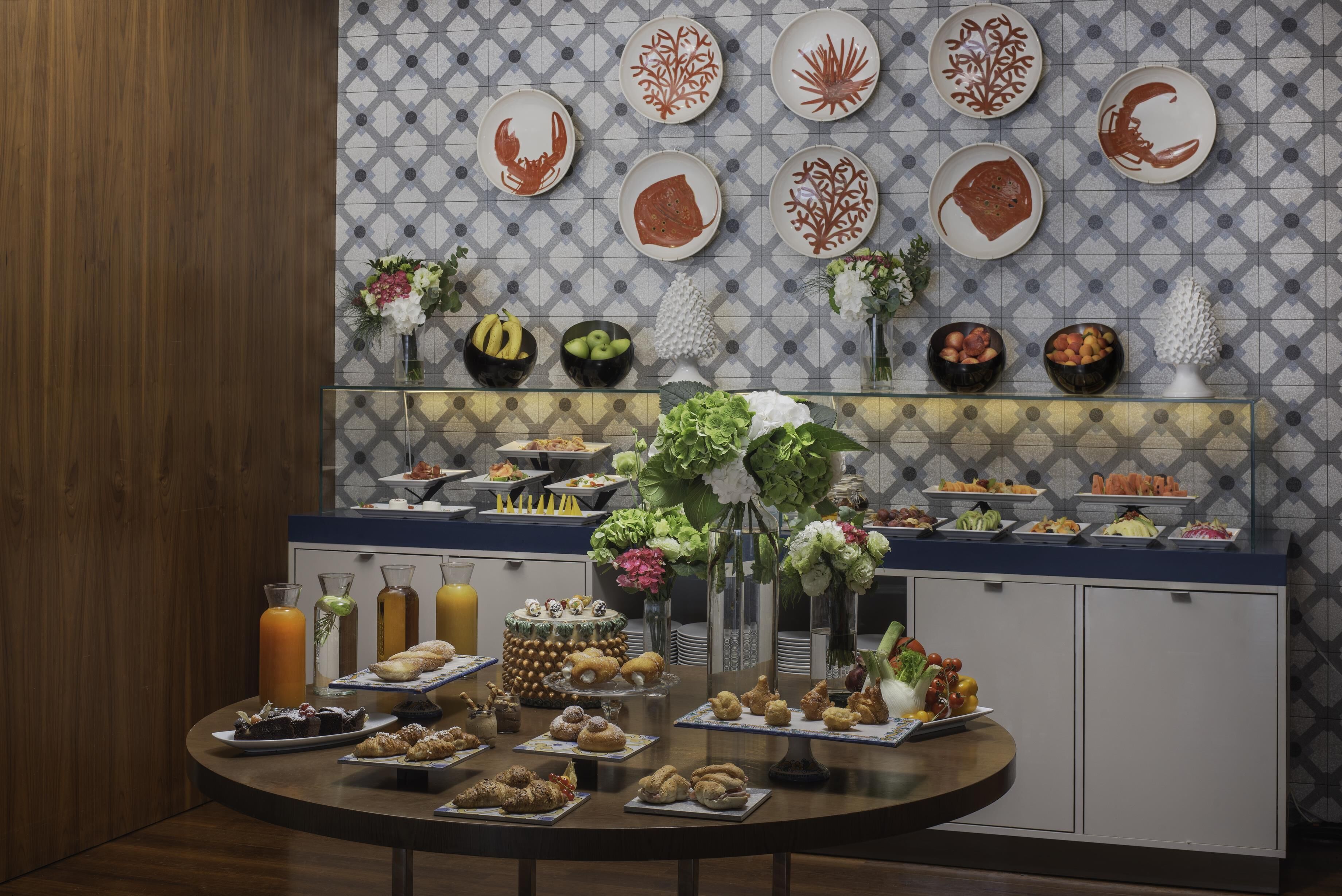 Un bufé de desayuno con diversos alimentos y una pared decorativa con platos.