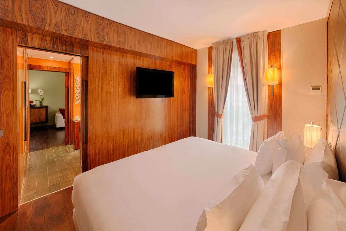 A hotel room with a large bed, wooden paneling, a flat-screen TV mounted on the wall, and a bathroom visible through an open door.