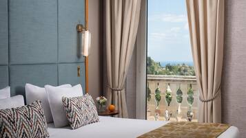 Habitación de hotel con cama, almohadas, mesita de noche, un jarrón con flores y vistas a un balcón con barandilla.