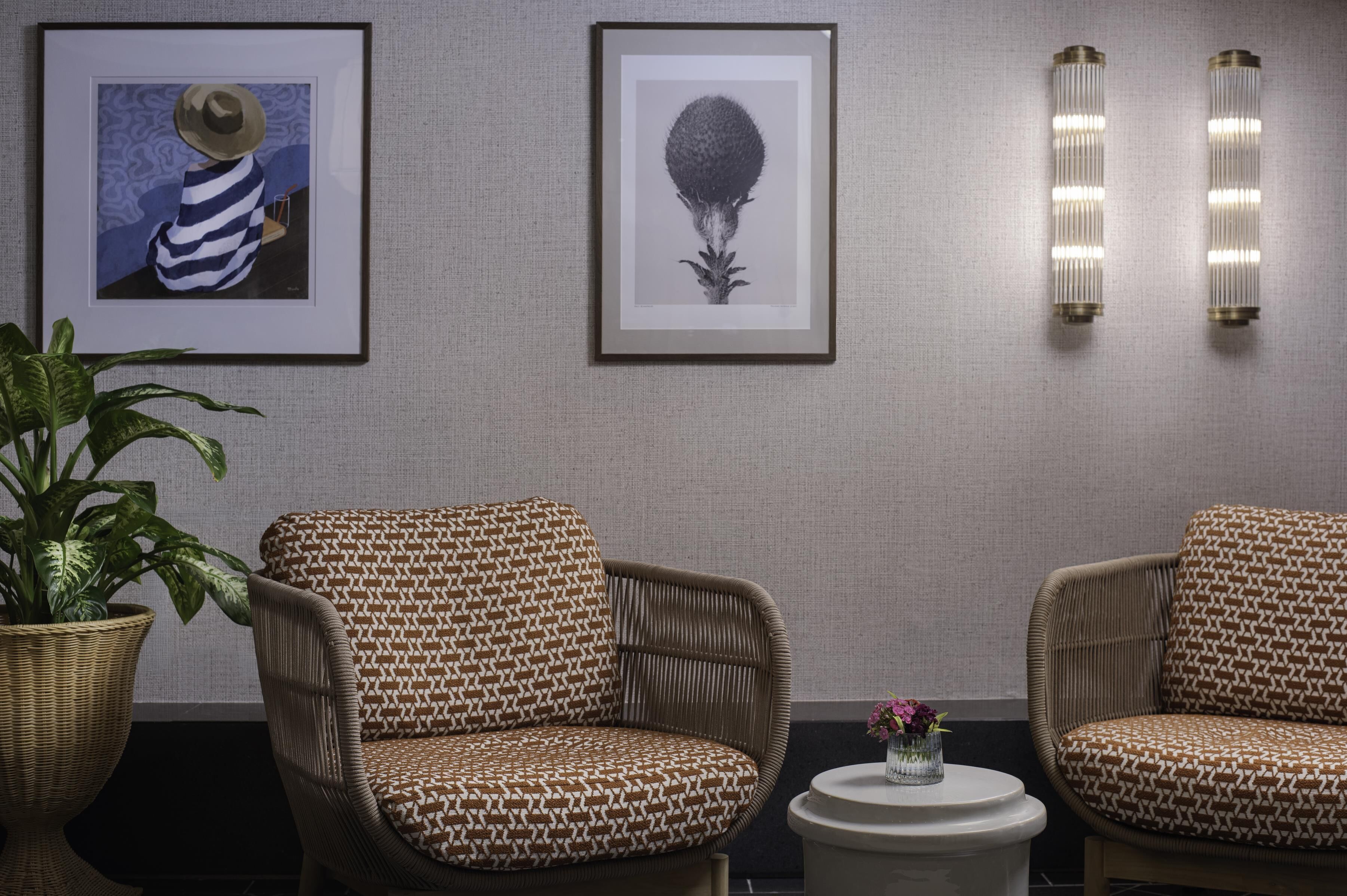 Une pièce comprenant deux fauteuils en osier, une petite table ronde et deux appliques murales.