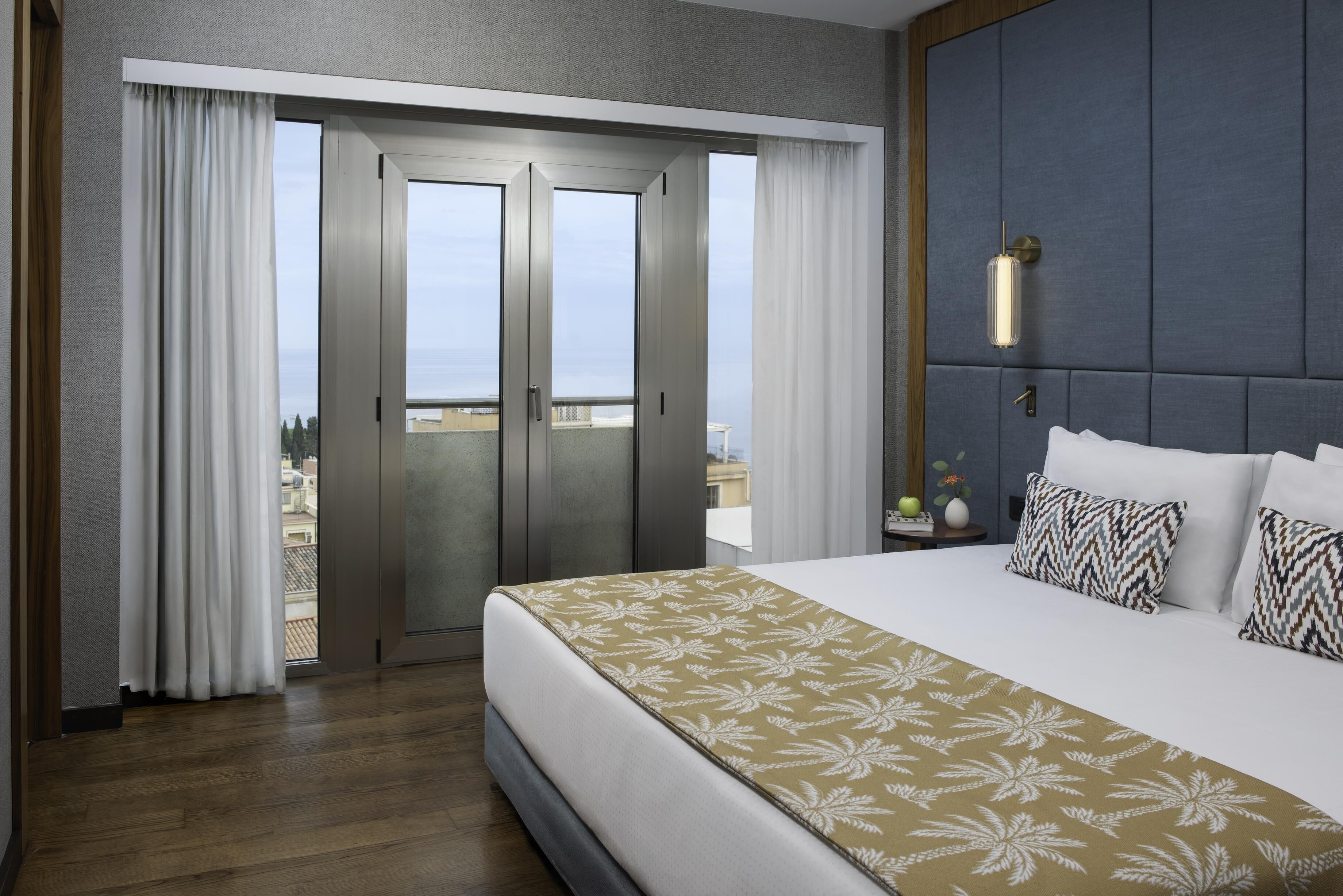 Una camera d'albergo con un letto grande, vista mare e un balcone con tende.