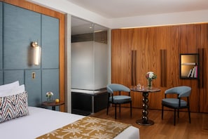 A hotel room with a bed, two chairs, a small table, a nightstand, and a wooden panel wall. - NH Collection Taormina (Taormina)