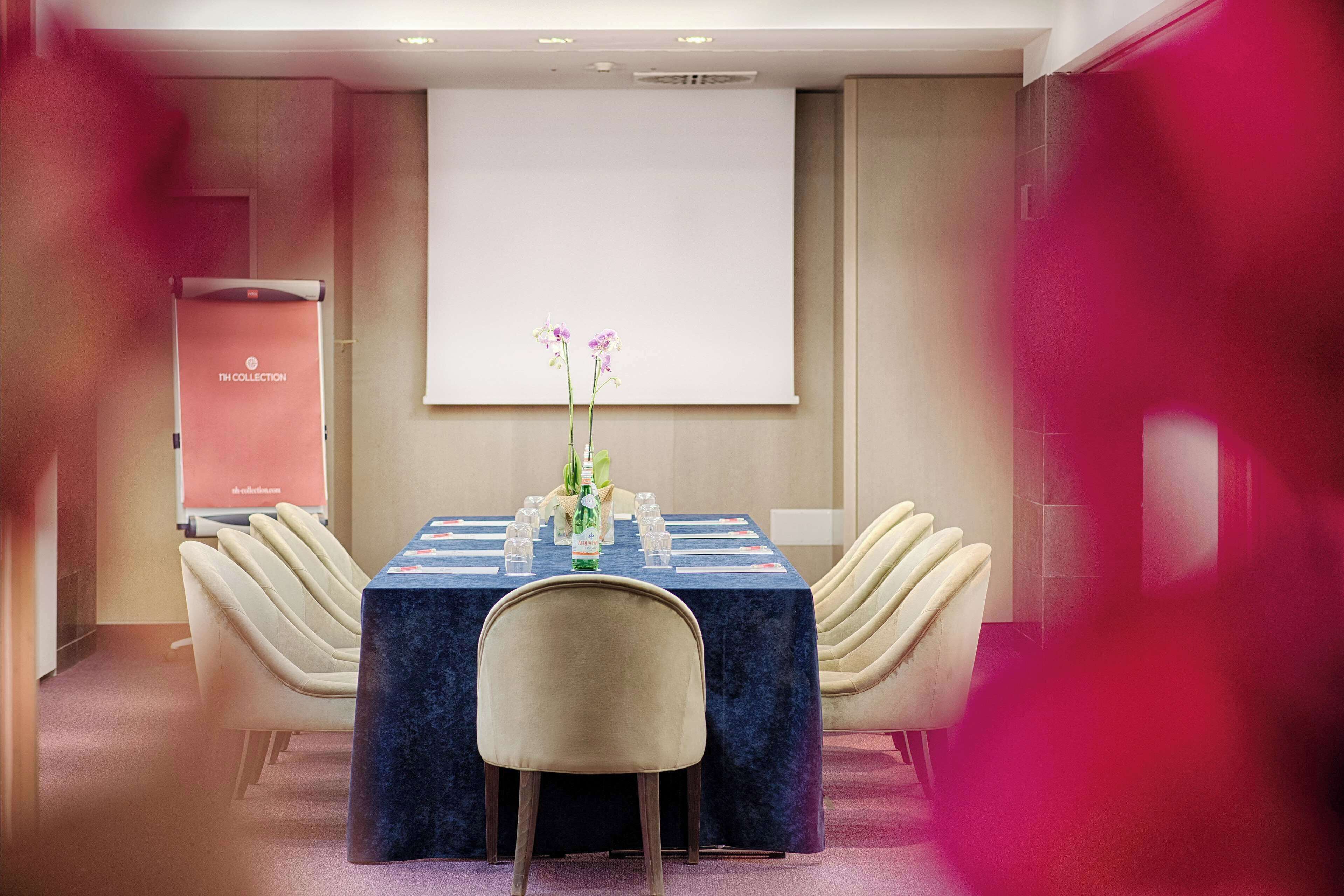 Une salle de conférence avec une longue table, des chaises de couleur beige, un écran de projection et un arrangement floral.