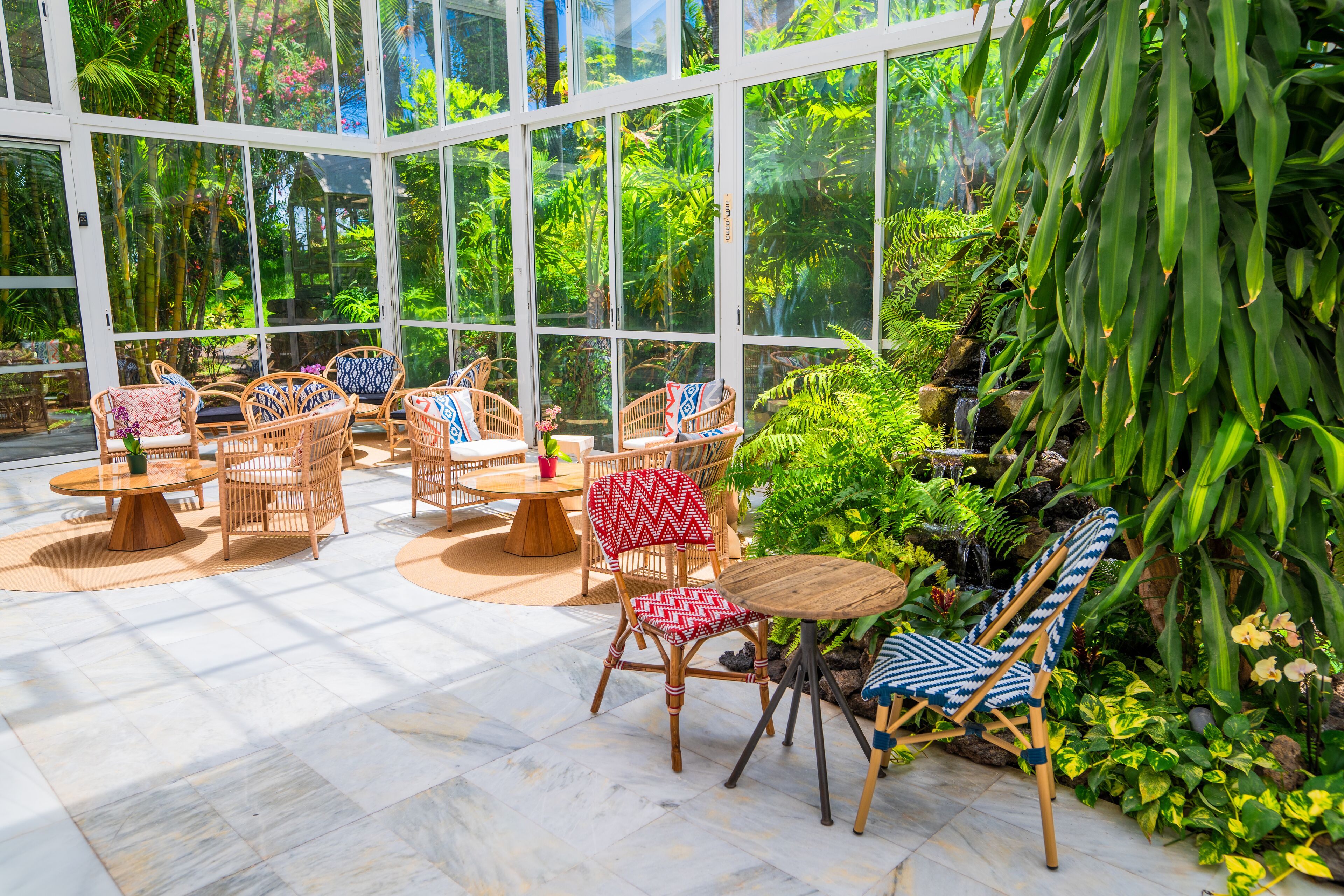 A conservatory with wicker furniture, a glass ceiling, and lush tropical plants.