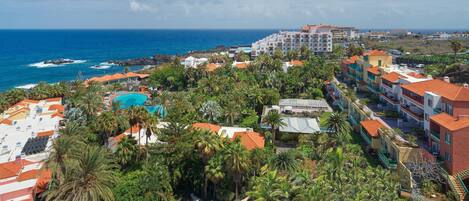 A coastal resort with a swimming pool, multiple-story buildings, and a view of the ocean.