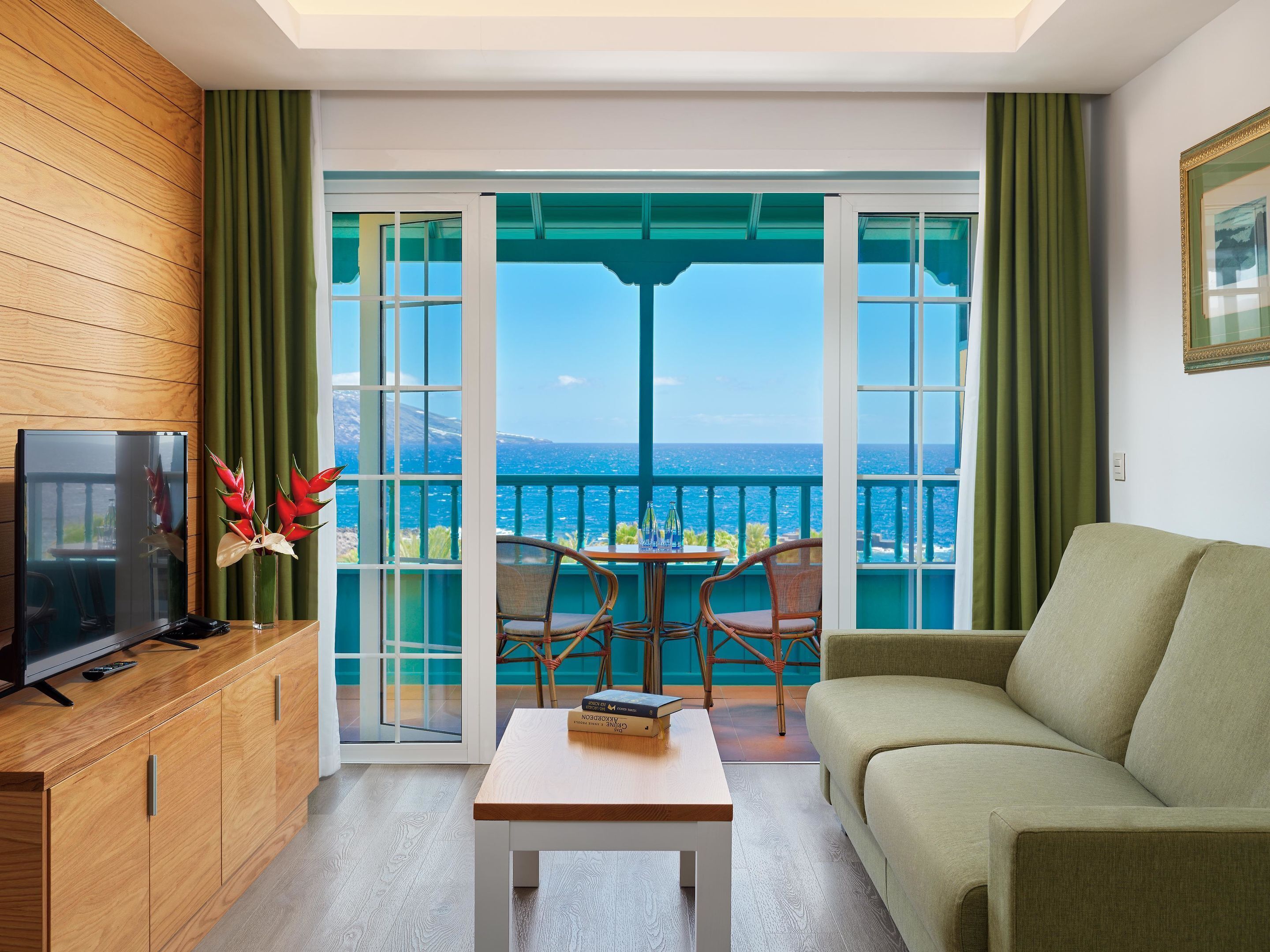 Ein modernes Wohnzimmer mit einem Holzkabinett, einem Flachbildfernseher, einem Couchtisch, einer Couch und einem Balkon mit Meerblick.