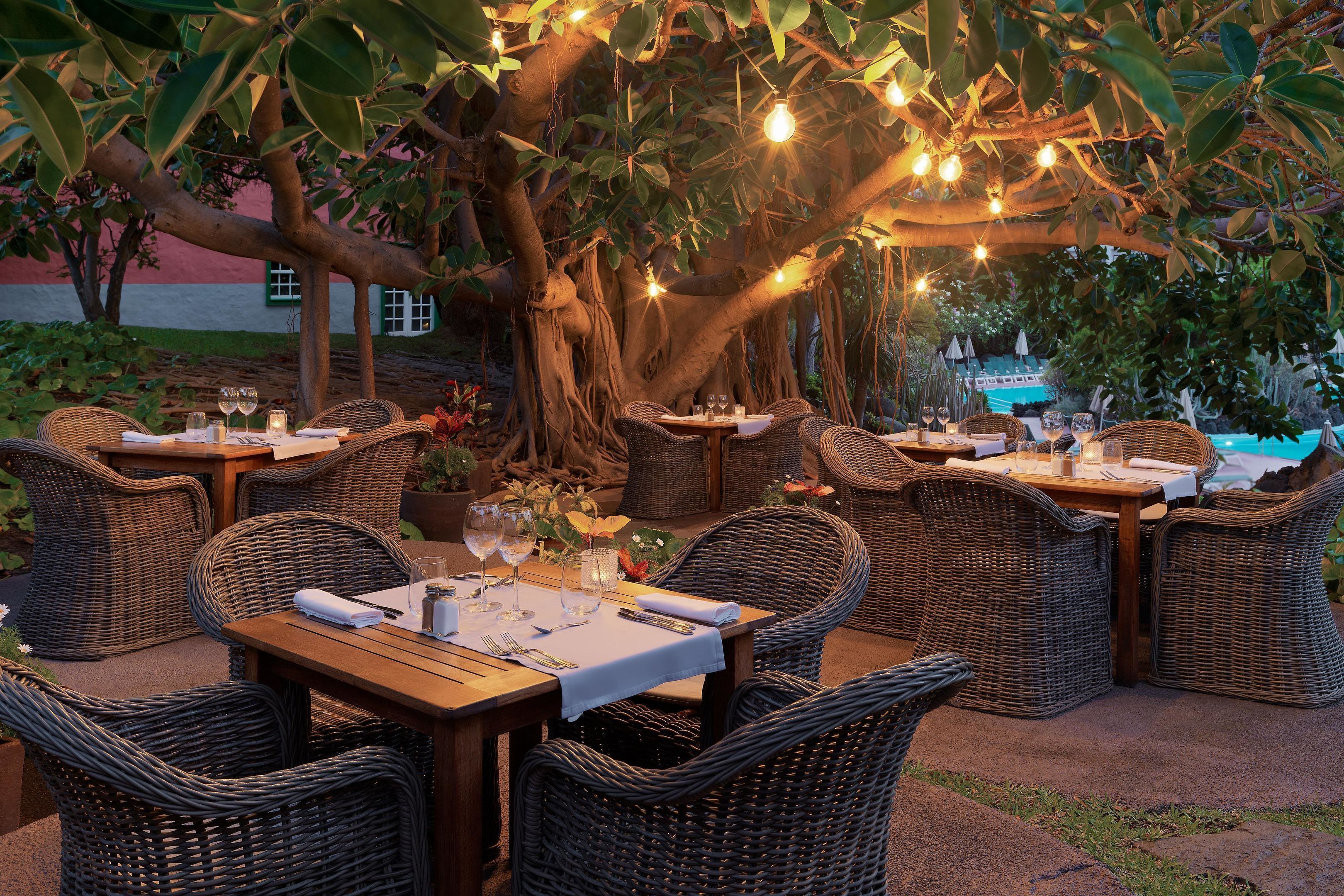 Un área de comedor al aire libre con mobiliario de mimbre y luces colgantes.