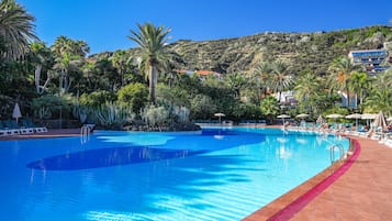 Una gran piscina con agua azul cristalina, rodeada de palmeras y un paisaje montañoso.