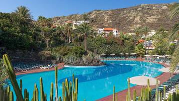 Una piscina rodeada de cactus y palmeras, con vistas a una ladera y edificios al fondo.