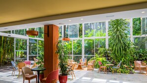 Un espacio interior amplio con ventanas grandes, mobiliario de mimbre y plantas en macetas.