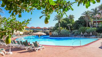 A swimming pool with lounge chairs and umbrellas, surrounded by palm trees and other greenery.