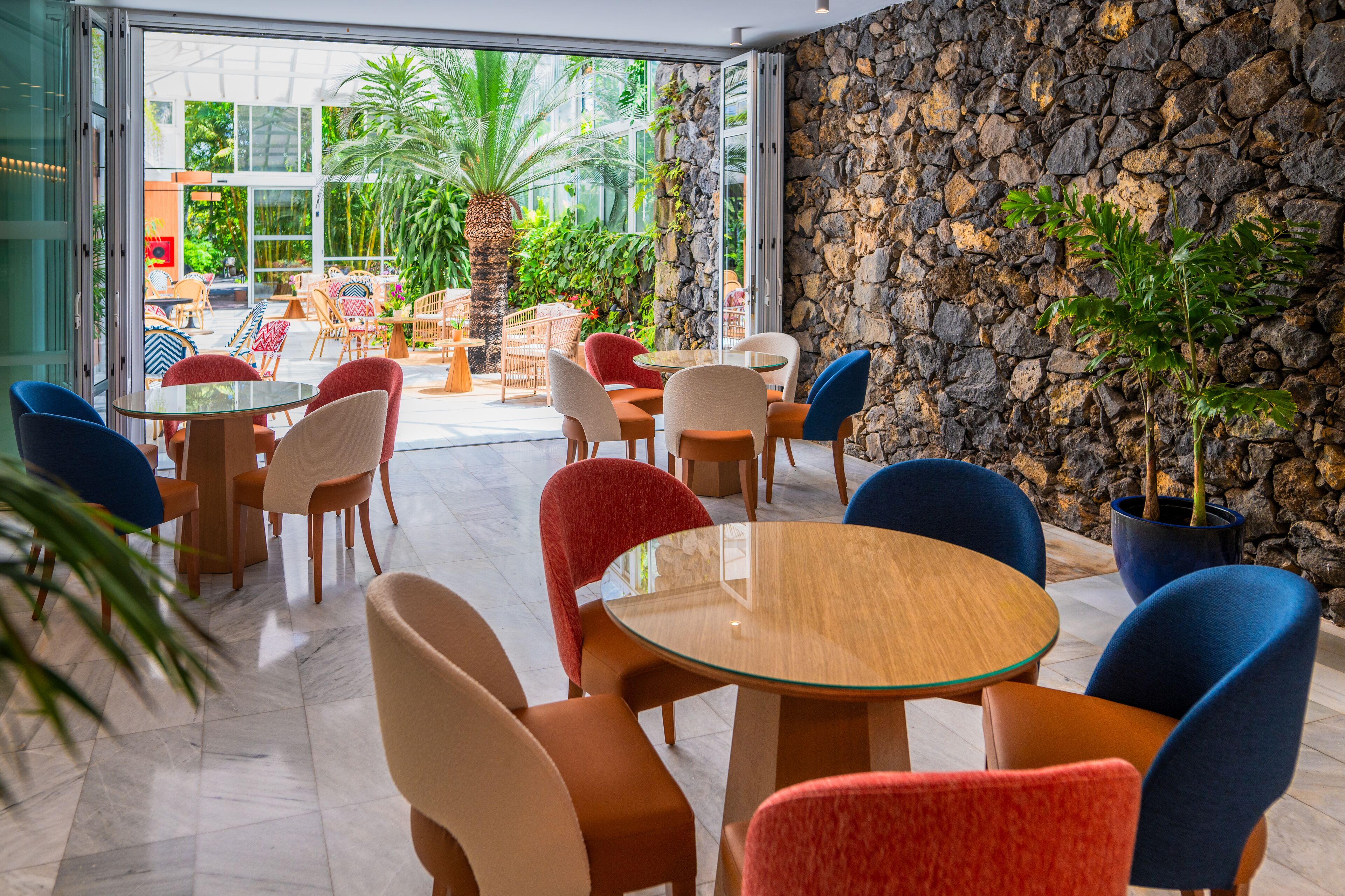 An indoor seating area with round tables and chairs, a stone wall, and potted plants.