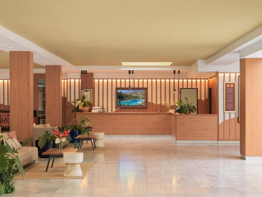 A modern hotel lobby with a reception desk, seating area, and a large TV screen.