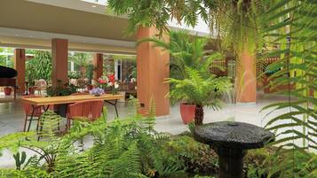 A spacious indoor area with a dining table, chairs, and a variety of potted plants, including ferns and a large tree.