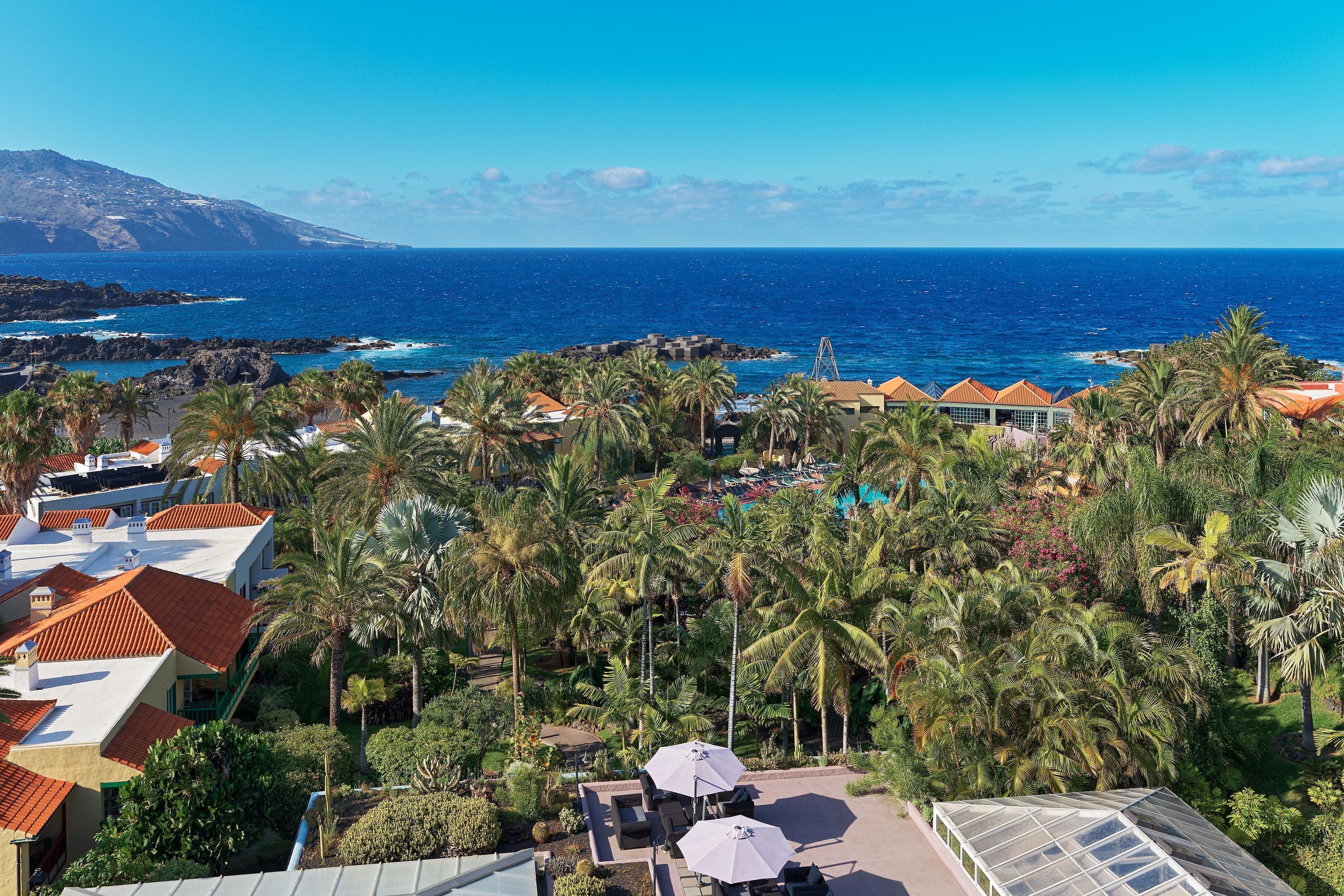 Un resort con vista al océano, palmeras y edificios de techo rojo.