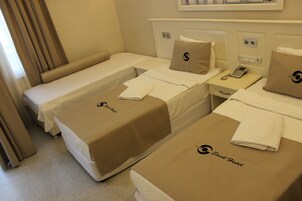 A hotel room with two single beds, each with a brown cover and a logo, a bedside table with a phone, and a window with curtains.