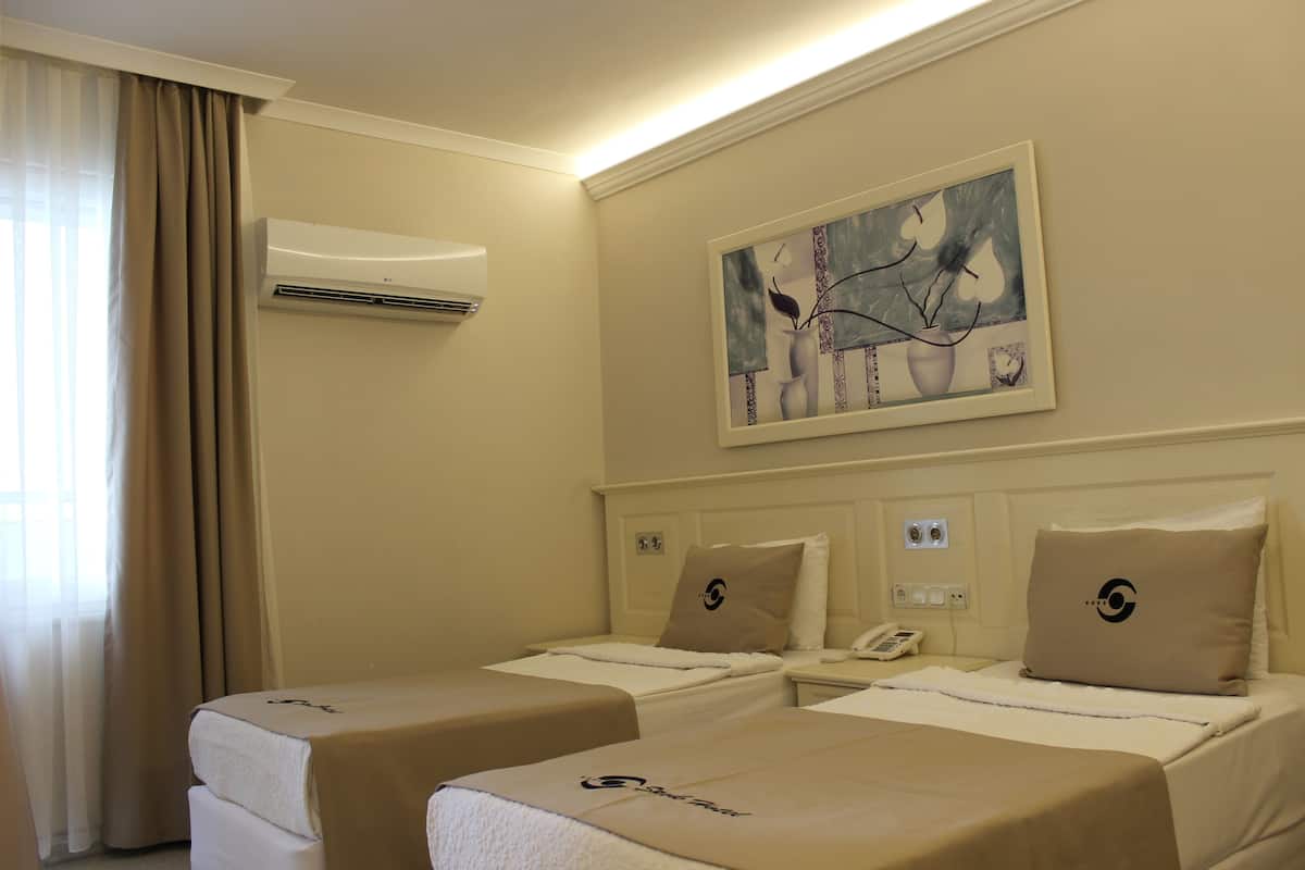 A hotel room with two beds, a painting on the wall, an air conditioning unit, and a window with curtains.