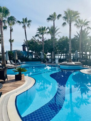A swimming pool with tiled edges, surrounded by palm trees and lounge chairs. - Savk Hotel (Alanya)