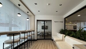 Un espacio de oficina moderno con una barra alargada, un área de estar con sofá y un comedor con pared de ladrillo y televisor.
