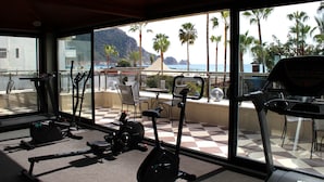 Un gimnasio con equipo de ejercicio y vistas al océano y palmeras.