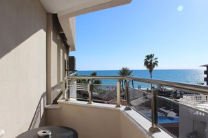 A balcony with a view of the sea, a palm tree, and outdoor furniture.