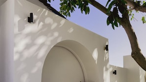 Un espacio moderno al aire libre con un banco curvo y una mesa redonda, rodeado de paredes blancas y un árbol.