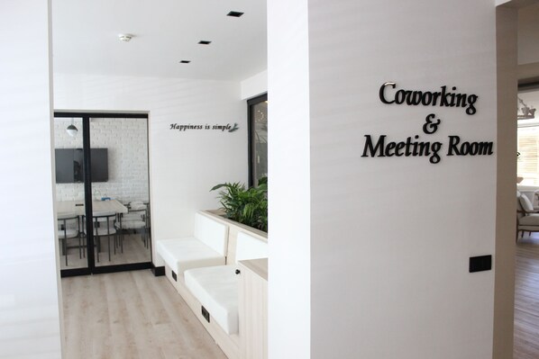 A modern workspace with a sign reading "Coworking & Meeting Room," a glass door leading to a dining area, and a minimalist design with a plant on the wall. - Savk Hotel (Alanya)