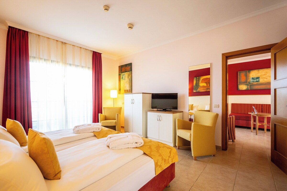 Ein Hotelzimmer mit zwei Betten, einem Schreibtisch, einem Fernseher und einer Sitzecke mit Stühlen und einem Sofa.