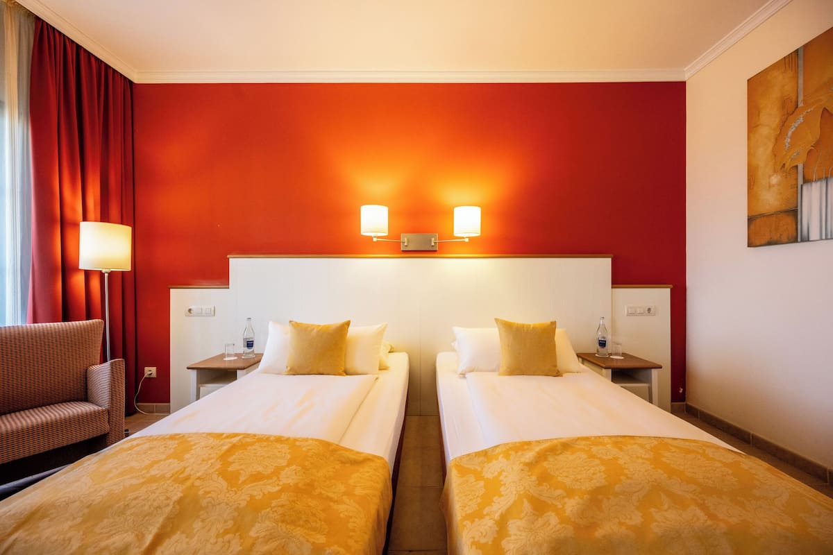 A hotel room with two beds, a sofa, a nightstand, and a lamp.