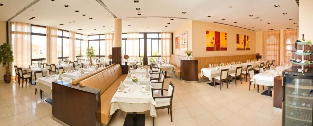 A spacious restaurant with multiple dining tables, a central seating area, and large windows allowing natural light.