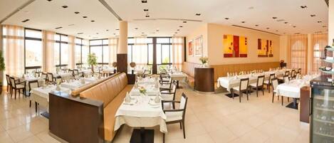 A spacious restaurant with multiple dining tables, a central seating area, and large windows allowing natural light.