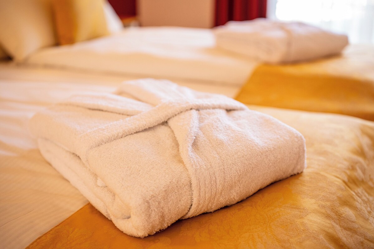 A neatly folded white towel on a wooden bed with a beige bedspread.
