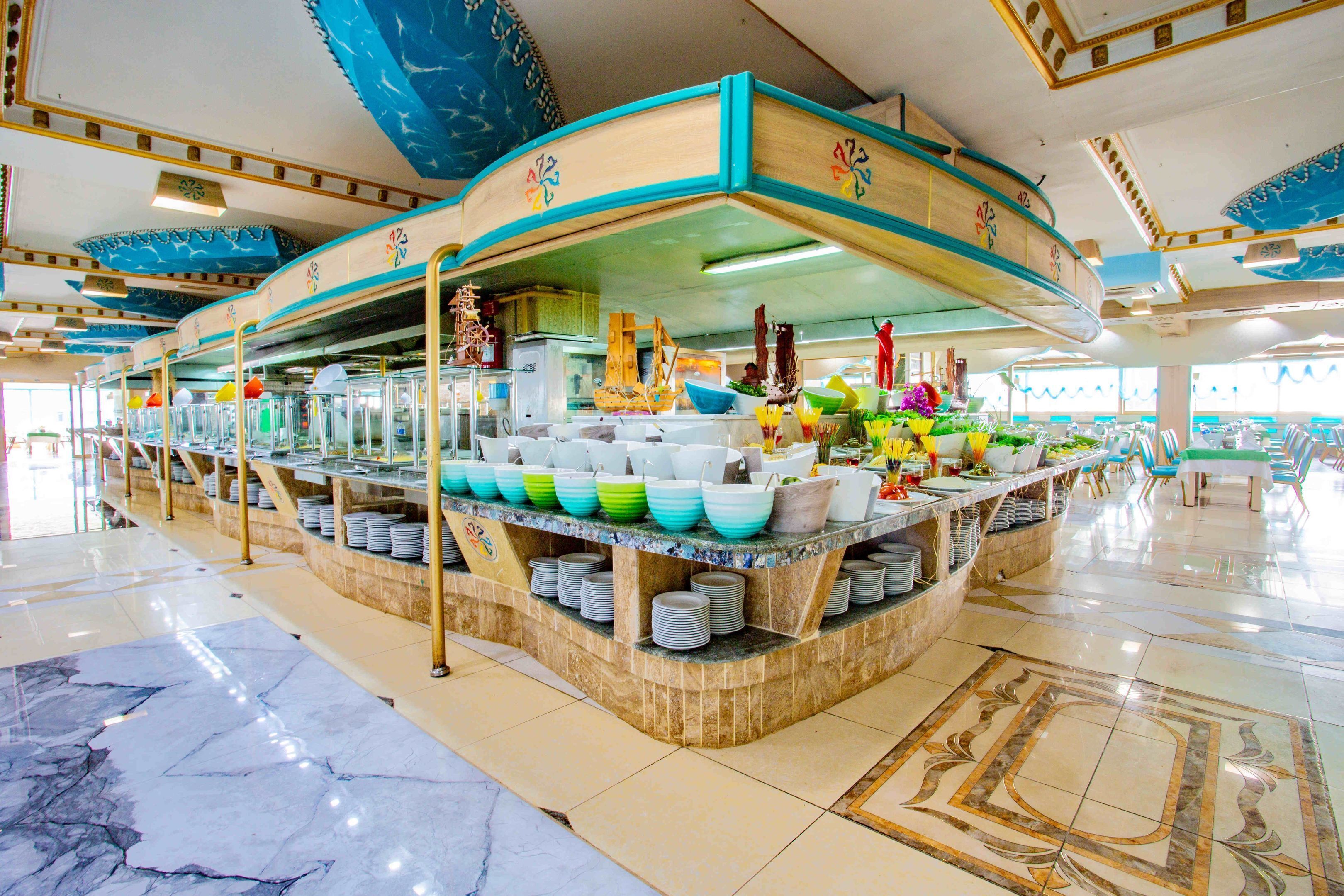 A buffet area with a central island surrounded by tables and chairs, featuring a variety of dishes and utensils.