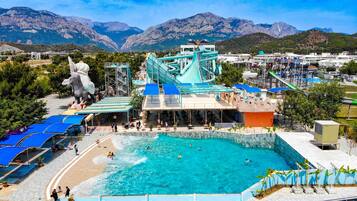 Un parque acuático con una piscina grande, toboganes y un telón de fondo montañoso.