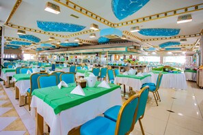 Une grande salle à manger avec de nombreuses tables et chaises, chacune recouverte d’une nappe verte et agrémentée de serviettes blanches.
