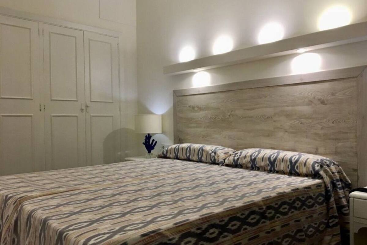 A bedroom with a patterned bedspread, a wooden headboard, and a bedside lamp.