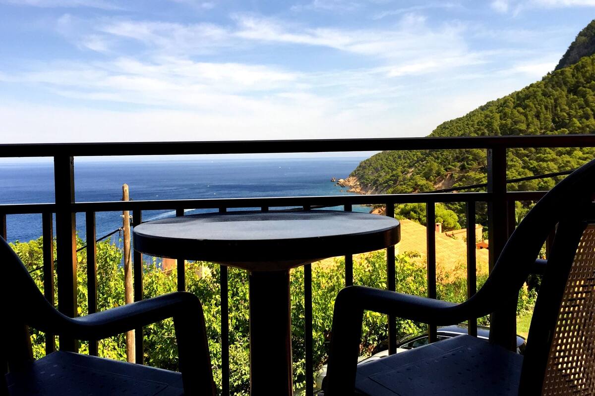 A balcony with a table and chairs overlooking a coastal view.