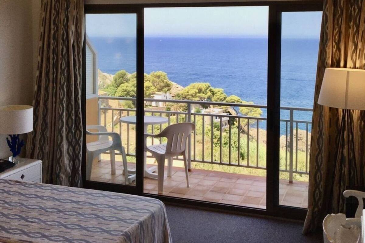 A hotel room with a large sliding glass door leading to a balcony with a view of the ocean.