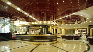 A hotel reception area with a curved counter, a reception desk, and a waiting area with sofas. - Sealine Hotel (Alanya)
