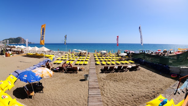 A beach with rows of sun loungers and umbrellas, a wooden walkway, and a view of the sea. - Sealine Hotel (Alanya)